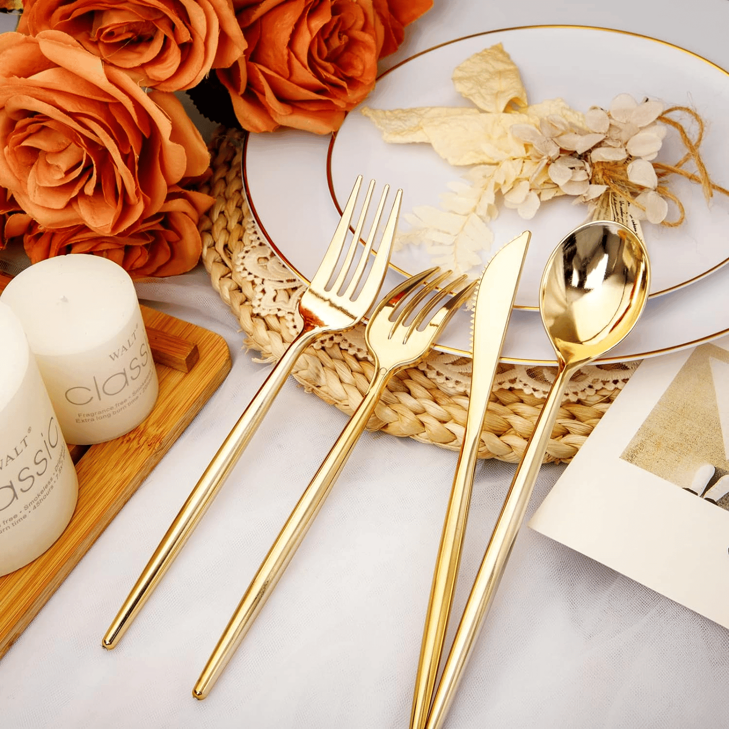 Gold plastic fork, knife and spoon with slim handles beside a white plate and orange roses