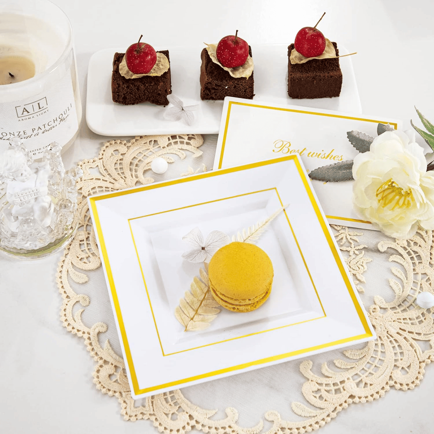 Square plastic dessert plate with a gold rim holding a macaron, beside brownie bites on a lace doily