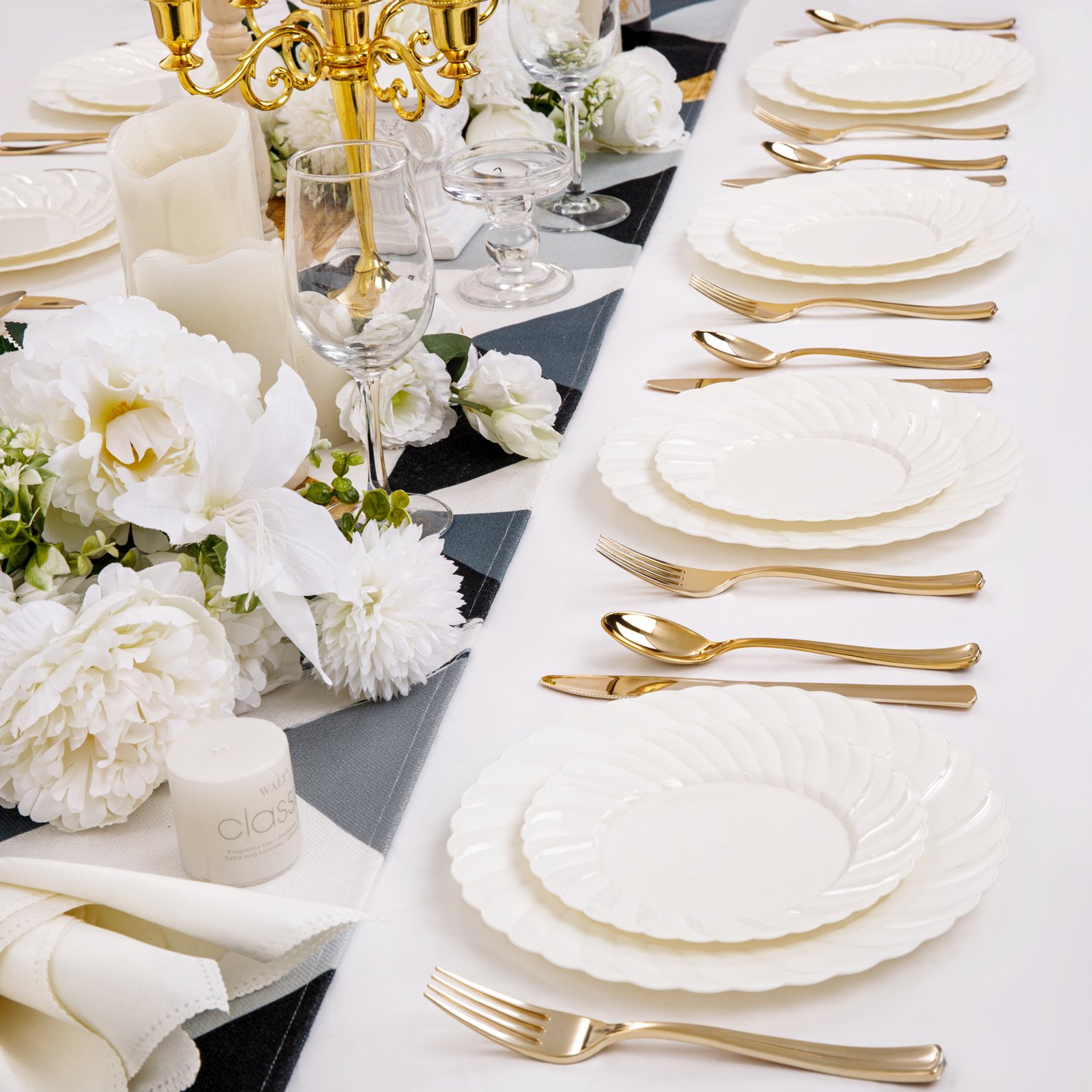 Ivory scalloped plastic plates and gold cutlery along a long banquet table with white flowers