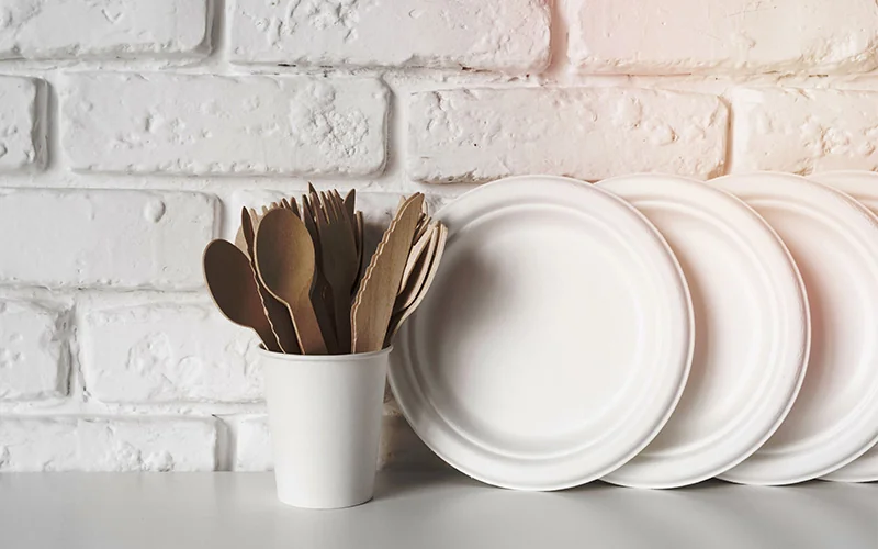 White disposable plates and wooden cutlery against a brick wall