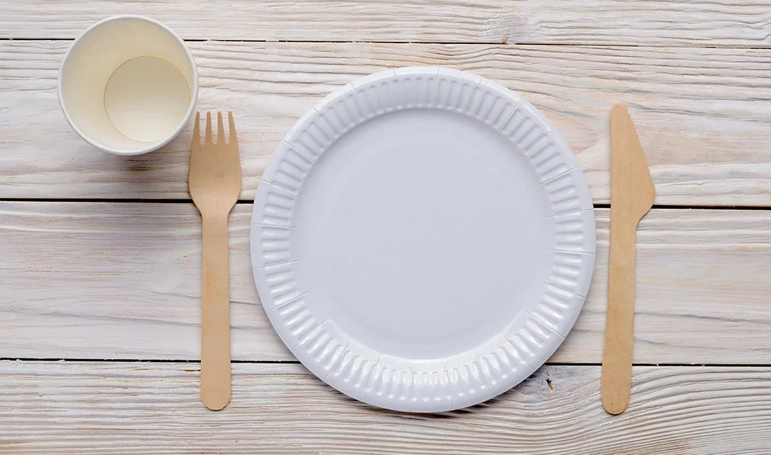 White disposable plate with wooden cutlery on a wood table